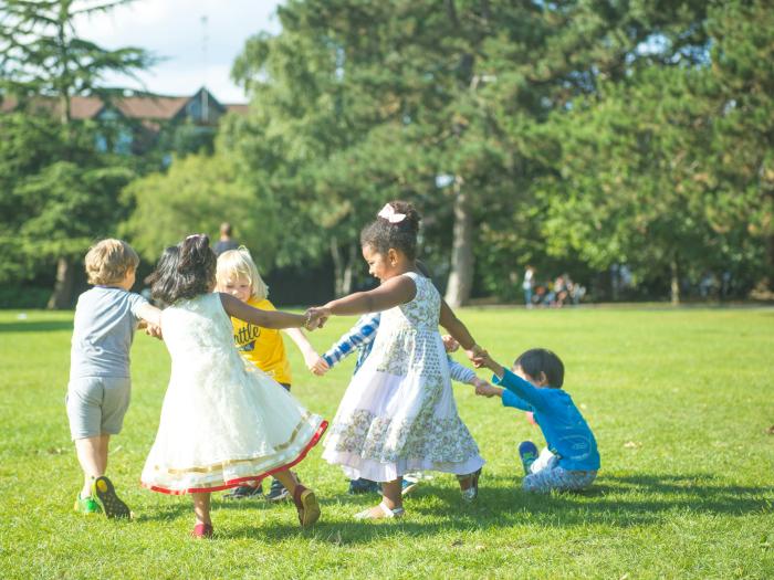 Young children holding hands in a circle formation outdoors in a park