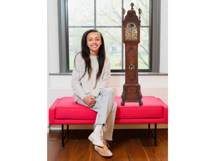 A smiling young woman, wearing light-colored clothes, sits on a red bench before a window next to a floating image of a tall, ornately decorated old clock.