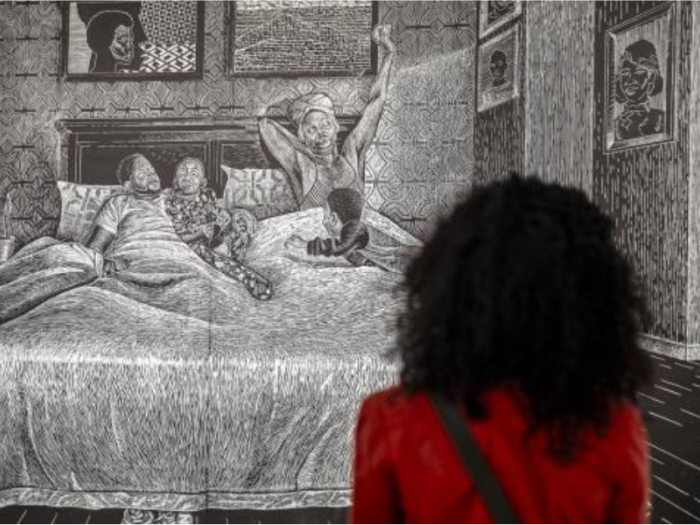 A person looking at a black and white woodcut print depicting a family waking up in a large bed.