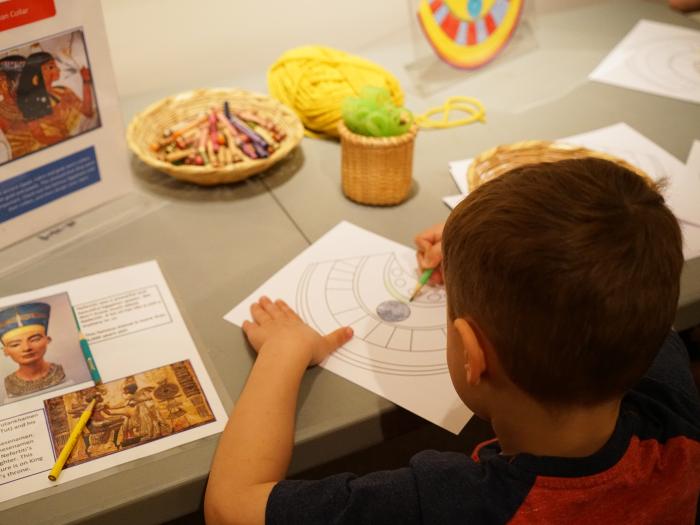 A child colors in an outline of an Egyptian collar.